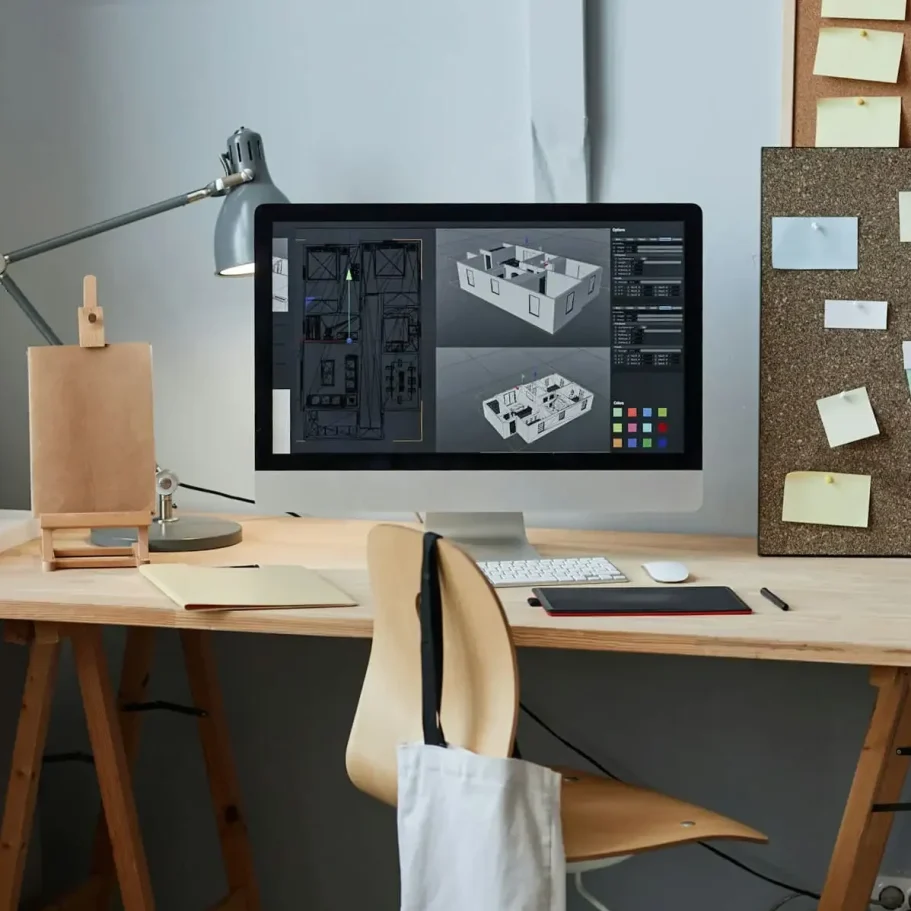 Schreibtisch mit Computer, Notizen, Skizzen eines Architekturmodells und einem Lampenlicht.