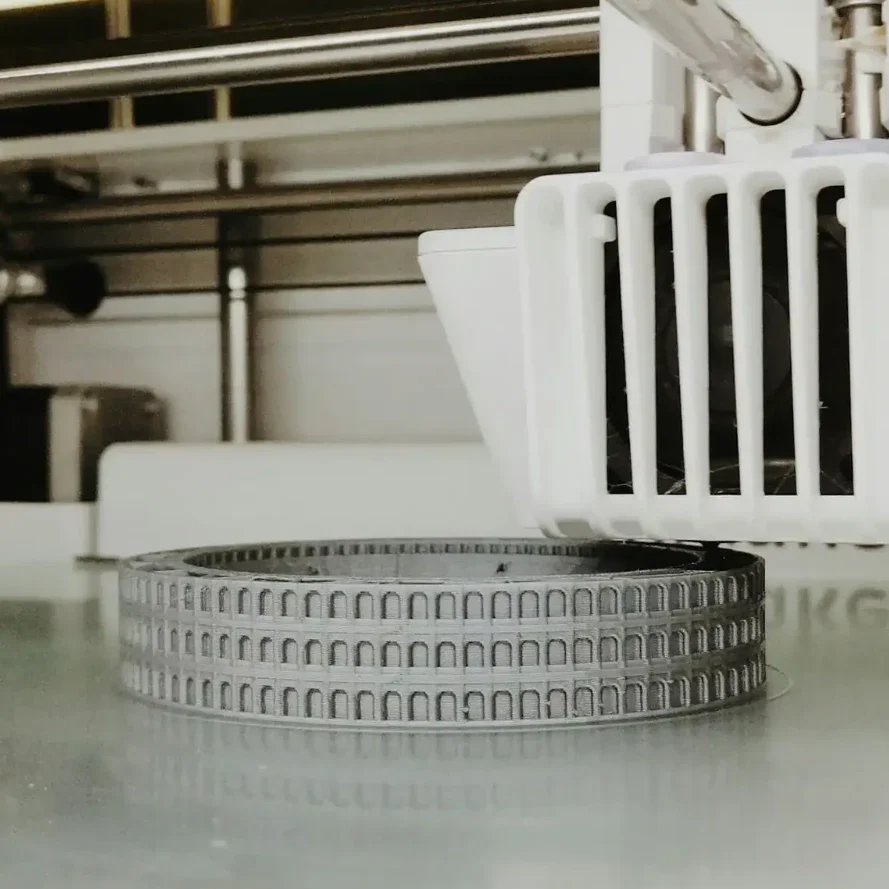 Graues Architekturmodell auf einem Tisch unter einem 3D-Drucker.