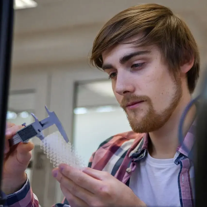 Eine Person misst mit einem Messschieber ein durchsichtiges 3D-Objekt in einem Lab.